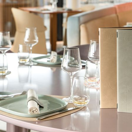 An elegantly laid light-colored table with a menu and wine glasses.